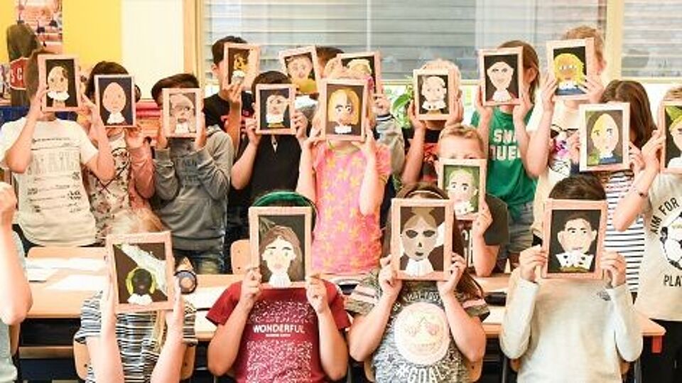 Kinderen in schoolklas met een getekend schilderijtje met een gezicht voor hun gezicht